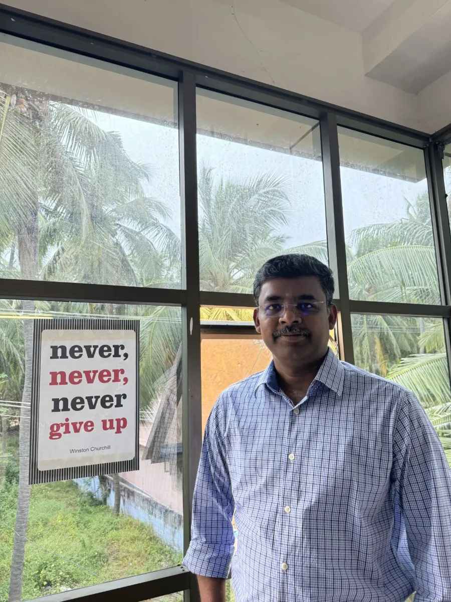 Sreedharan beside a sign reading never, never, never give up